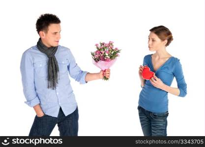 Young attractive couple in love. Woman giving her heart, man offering flowers, isolated on white background.