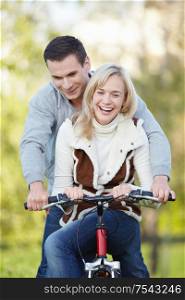 Young attractive couple rides a bicycle in the park
