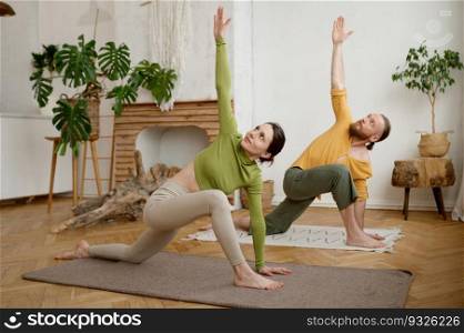 Young attractive family coup≤practicing yoga stretχng standing in Utthita Parshvakonasana pose. Workout at home, hea<hy lifesty≤and body care concept. Young attractive family coup≤practicing yoga stretχng workout at home