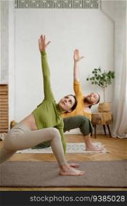 Young attractive family couple practicing yoga stretching standing in Utthita Parshvakonasana pose. Workout at home, healthy lifestyle and body care concept. Young attractive family couple practicing yoga stretching workout at home