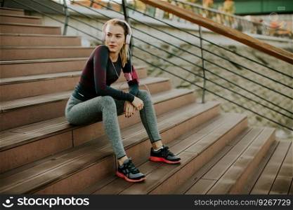 Young attractive female runner taking break after jogging outdoors