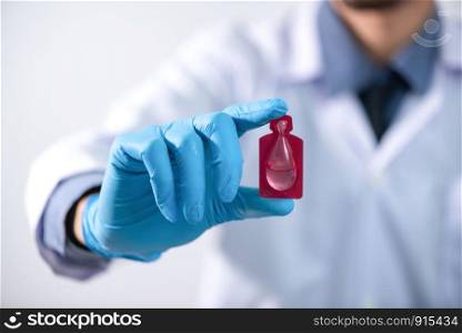 Young attractive female scientist with protective eyeglasses and mask holding a transparent pill with fingers in gloves in the pharmaceutical research laboratory