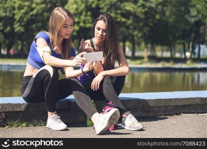 Young attractive fitness girls talking about their workout and checking sport application details on the smartphone (vintage effect)