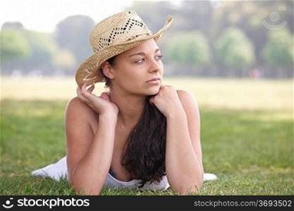 young attractive girl lying on grass contemplating while wearing a summer hat