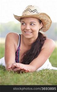 young attractive girl lying on grass wearing a summer hat