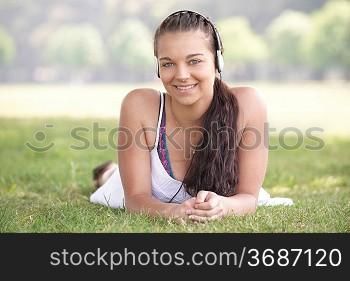 young attractive girl lying on grass wearing headphones while listening to music