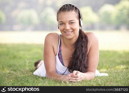 young attractive girl lying on grass wearing headphones while listening to music