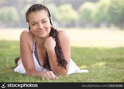 young attractive girl lying on grass wearing headphones while listening to music