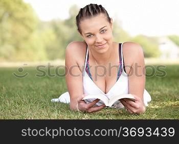 young attractive girl lying on grass while reading a book