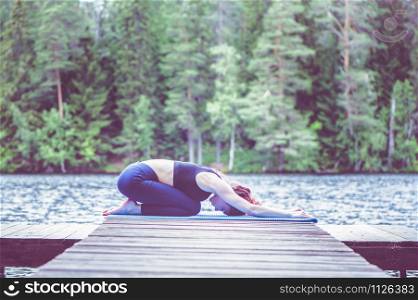 Young attractive girl practicing yoga, sitting in Child exercise, Balasana pose on the lake. The concept of appeasement, healthy lifestyle