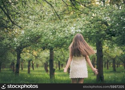Young attractive girl running in the garden, view from the back