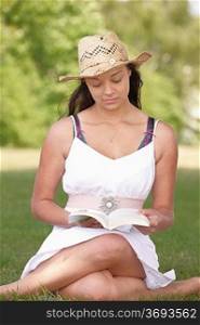 young attractive girl sitting on grass while reading a book