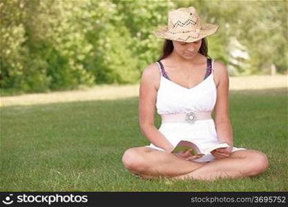 young attractive girl sitting on grass while reading a book