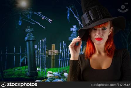 young attractive green-eyed red-haired witch in a classic pointed hat on a background of a gloomy cemetery. dark toy cemetery