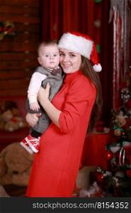 Young attractive happy mother have a good time with her son at home near christmas tree. Family, happiness, holidays, new year concept. Young attractive happy mother in santa’s hat have a good time with her son at home near christmas tree. Family, happiness, holidays, new year concept