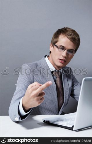 Young attractive man in a suit with the laptop shows an obscene sign to the camera