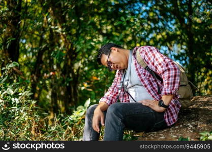 young attractive man with travel backpack feeling tried after hiking at nature and fresh environment on trekking journey, sitting for rest on rocky and wipe sweat in forest, copy space