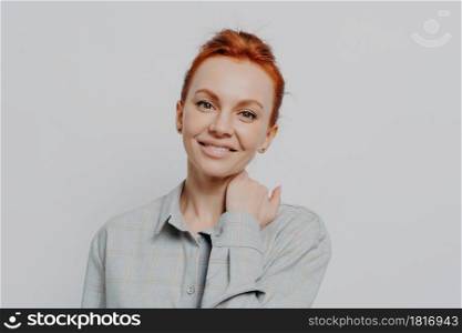 Young attractive smiling female with ginger hair in casual outfit isolated on grey studio background, happy caucasian woman with beaming smile looking at camera, posing indoors. Young attractive smiling female with ginger hair in casual outfit isolated on grey studio background