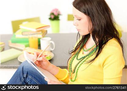 Young attractive student girl thinking and studying in kitchen