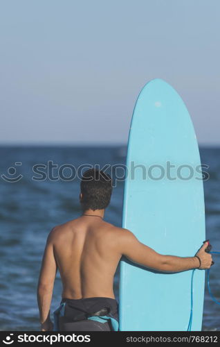 Young attractive surfer holding his surfboard at the beach