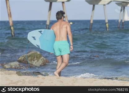 Young attractive surfer holding his surfboard at the beach