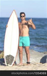 Young attractive surfer holding his surfboard at the beach wearing a green swimsuit