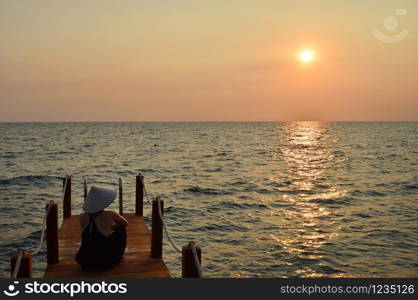 Young attractive woman at the seashore in Vietnam wearing a typical hat staring at the sunset.. Lonely girl watching the sunset in Vietnam.