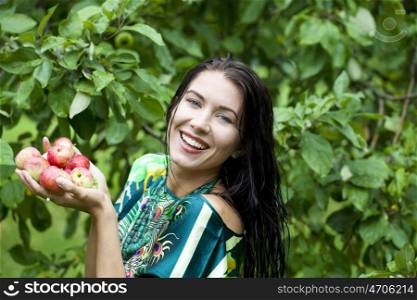 Young attractive woman holding apples, against green of summer park.