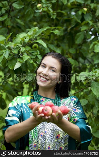 Young attractive woman holding apples, against green of summer park.