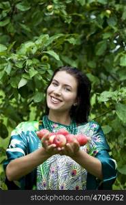 Young attractive woman holding apples, against green of summer park.