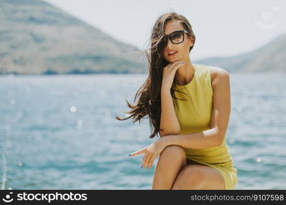 Young attractive woman in a yellow dress relaxing by the sea at sunny day