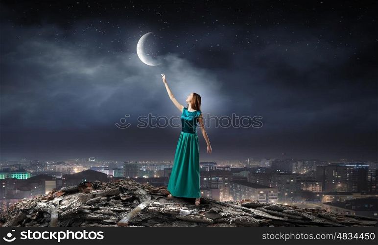 Young attractive woman in green dress reaching moon. Young romantic lady