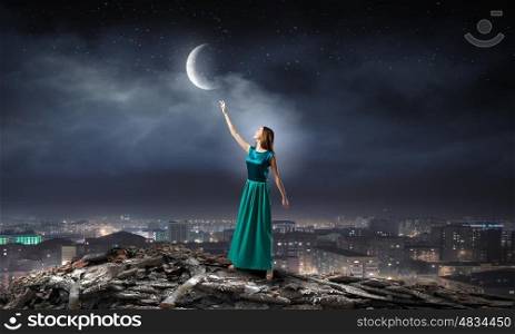 Young attractive woman in green dress reaching moon. Young romantic lady
