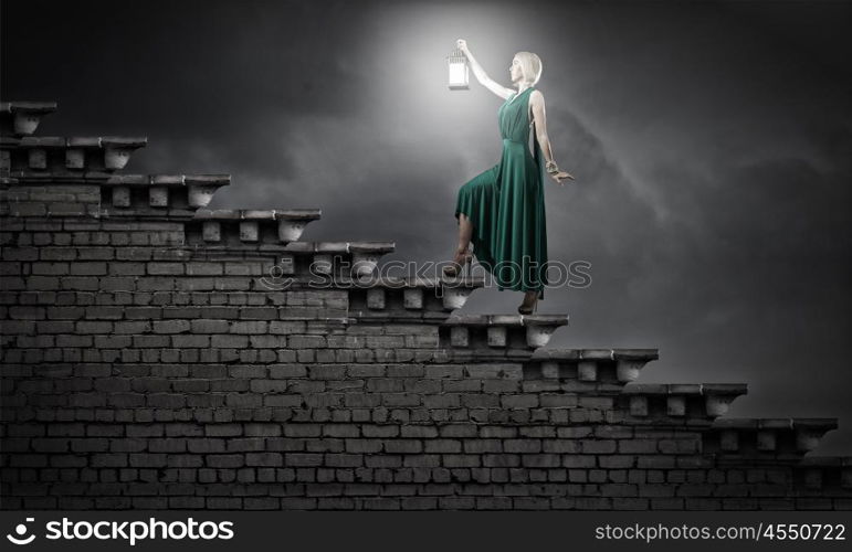 Young attractive woman in green dress with lantern walking in darkness. Lost in night