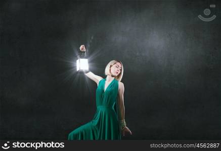 Young attractive woman in green dress with lantern walking in darkness. Lost in night