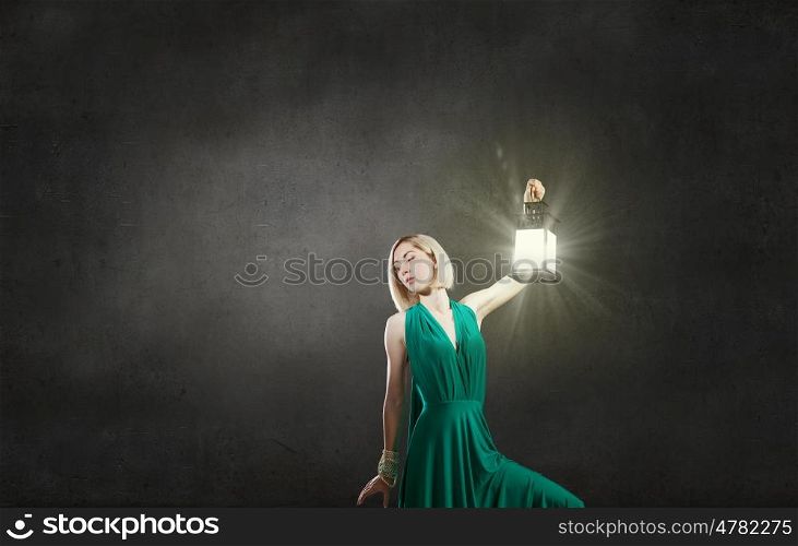 Young attractive woman in green dress with lantern walking in darkness. Lost in night