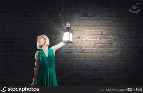 Young attractive woman in green dress with lantern walking in darkness. Lost in night