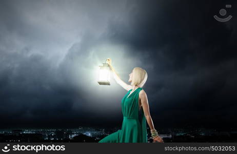 Young attractive woman in green dress with lantern walking in darkness. Lost in night