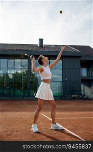 Young attractive woman in sportswear playing tennis outdoors. Pretty female holding racket training to serve ball at private club. Young attractive woman in sportswear playing tennis outdoors