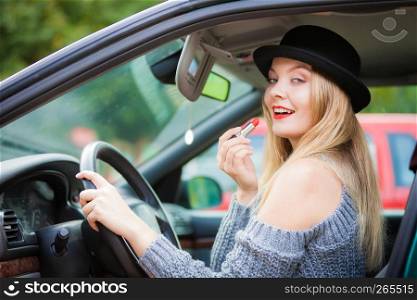 Young attractive woman looking in rear view mirror painting her lips doing applying make up while driving the car.. Young woman applying lipstick in car