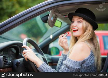 Young attractive woman looking in rear view mirror painting her lips doing applying make up while driving the car.. Young woman applying lipstick in car