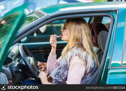 Young attractive woman looking in rear view mirror painting her lips doing applying make up while driving the car.. Young woman applying lipstick in car