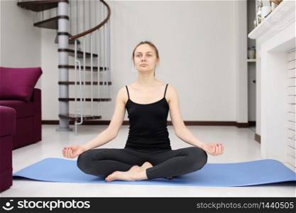 Young attractive woman practicing yoga, yoga studio. quarantine sports. Woman training and practicing yoga at class. Girl doing exercises at home