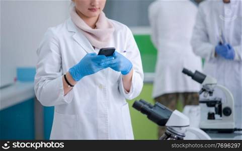 Young attractive woman scientist using smartphone in the scientific chemical laboratory