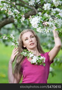 young attractive woman standing near the blossoming apple tree.