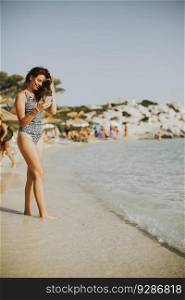 Young attractive woman walking on the beach and using a mobile phone in summer