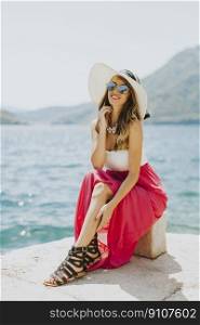 Young attractive woman with a hat and glasses poses by the sea at sunny day