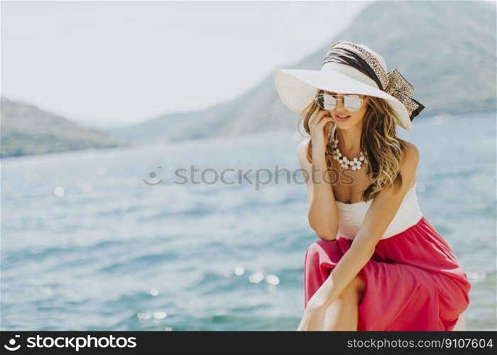 Young attractive woman with a hat and glasses poses by the sea at sunny day