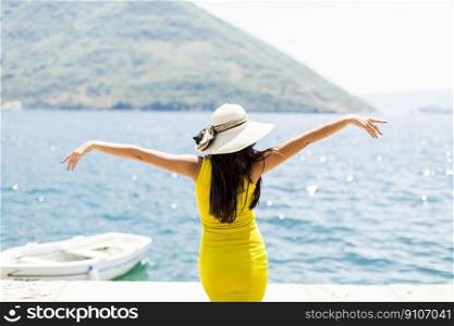 Young attractive woman with a hat poses by the sea at sunny day