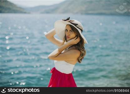 Young attractive woman with a hat poses by the sea in the summer